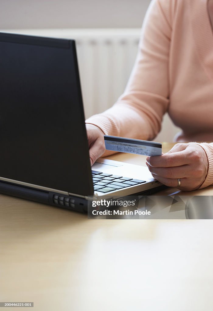 Woman using laptop computer, holding credit card, close-up