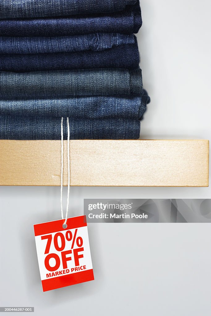 Sale tag attached to jeans piled on shelf display, close-up