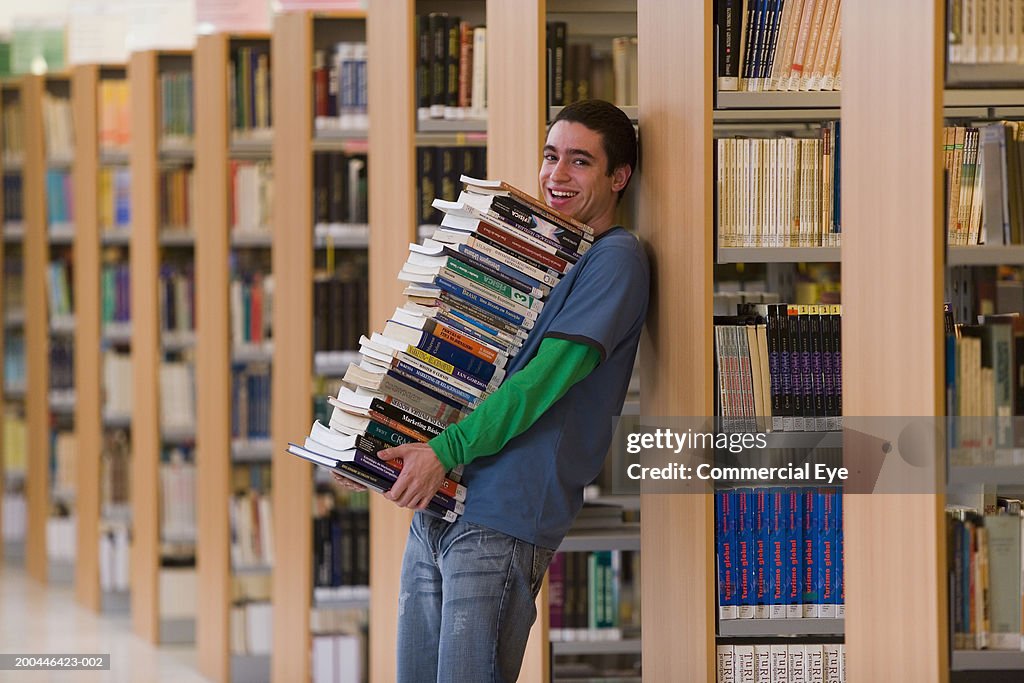 Student with stack of books leaning against bookcase, portrait