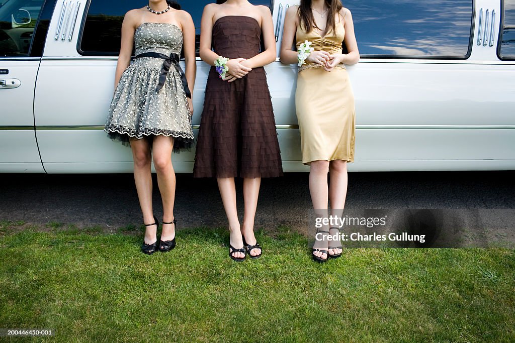 Three teenage girls (14-18) in formal dresses beside limo, low section