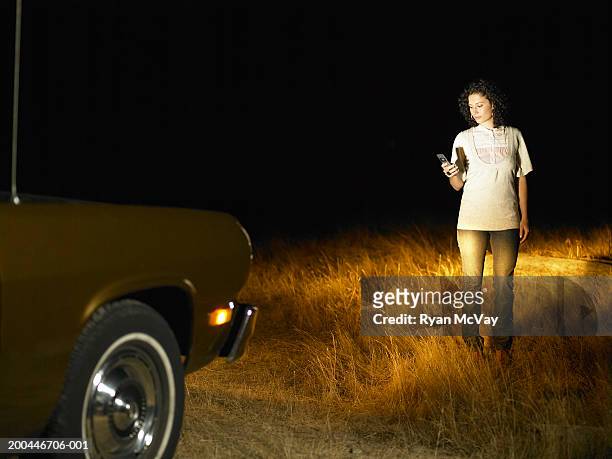 young woman using cell phone in front of parked car, night - mystery car stock pictures, royalty-free photos & images