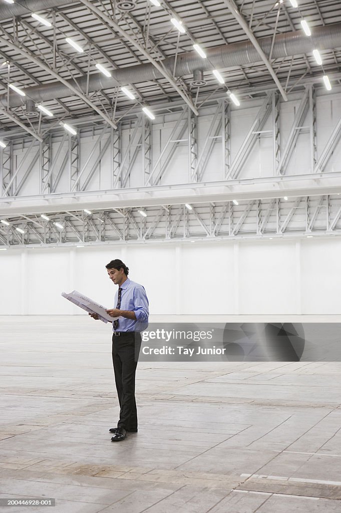 Businessman standing in empty warehouse holding plans