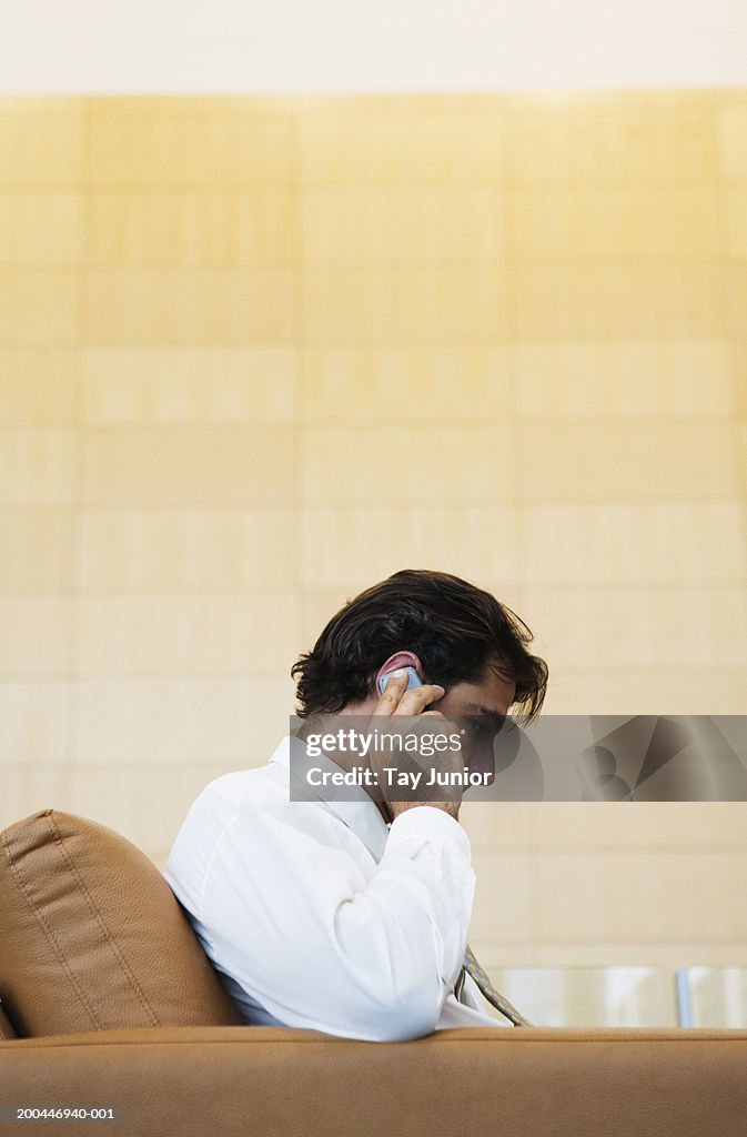 Businessman sitting in armchair using mobile phone, side view