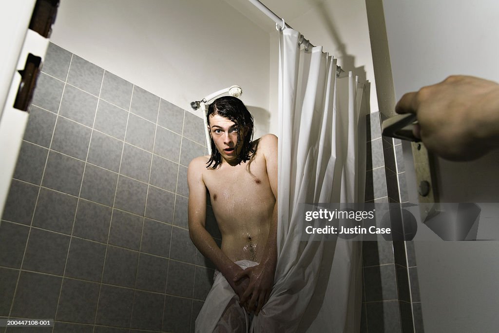 Young man in shower, shocked expression on face as person enters room
