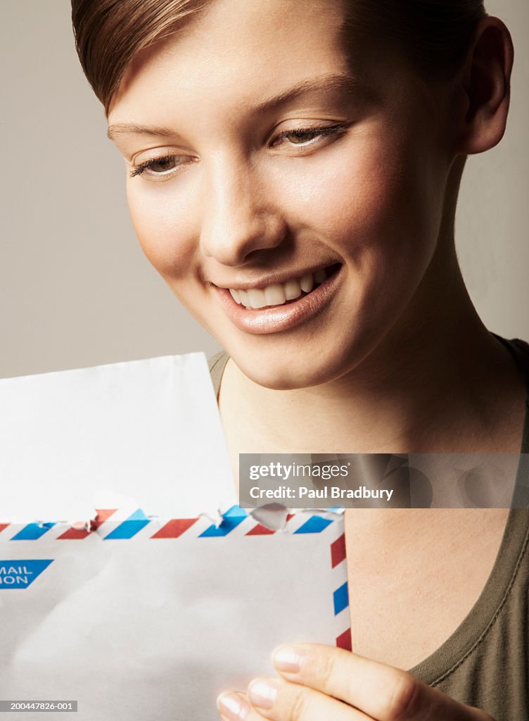 Young woman holding envelope, reading letter, smiling, close-up