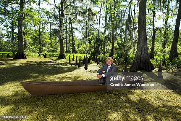 businessman wearing straw hat sitting in boat in swamp, portrait - louisiana swamp stockfoto's en -beelden