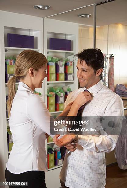 young woman fixing tie for man in clothes store, smiling - kraag stockfoto's en -beelden