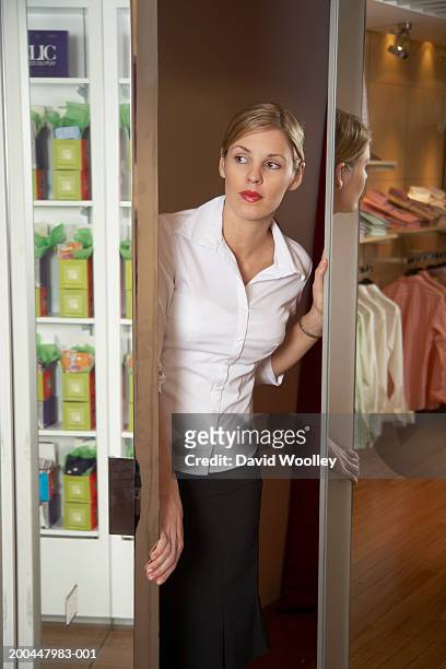 young woman looking out from between mirrored doors in clothes store - offener kragen stock-fotos und bilder