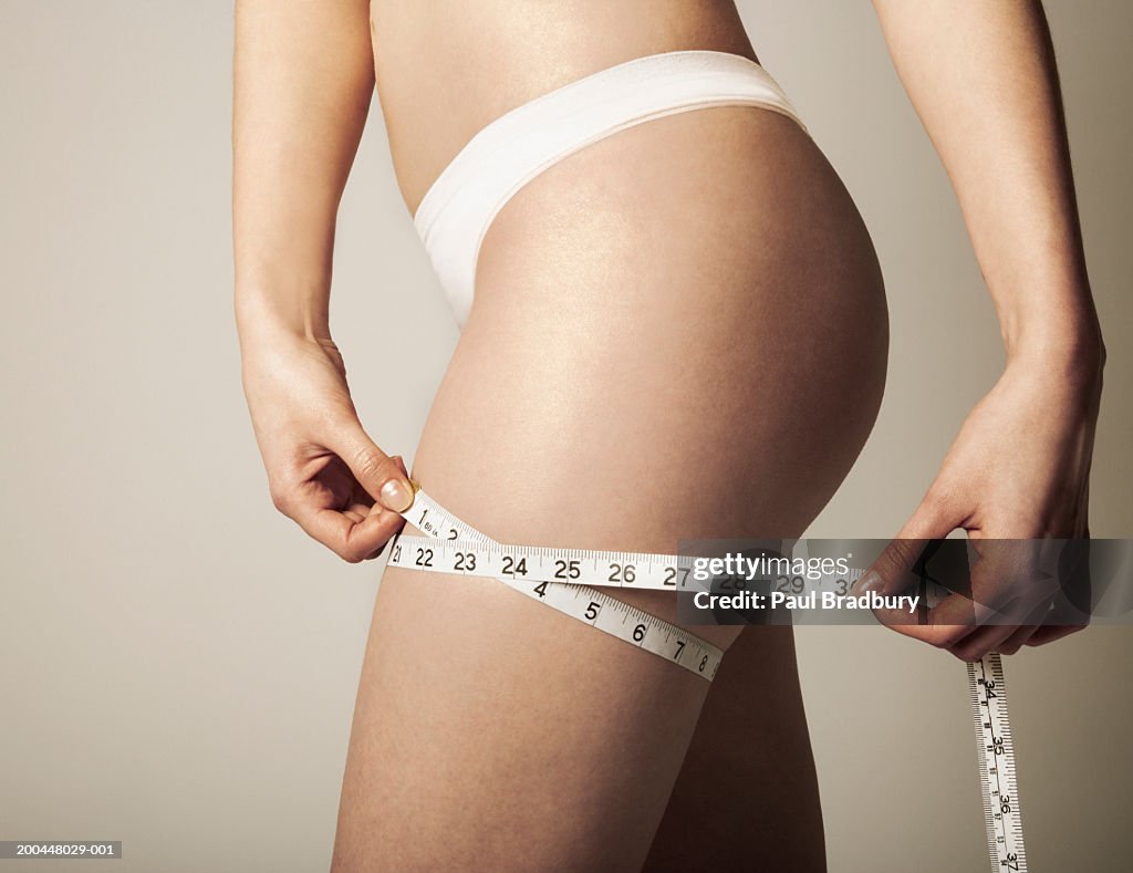 Woman holding measuring tape around thigh, mid section, side view