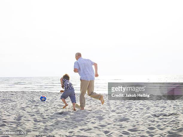 grandfather playing football on beach with grandson (4-6) rear view - boy barefoot rear view stockfoto's en -beelden