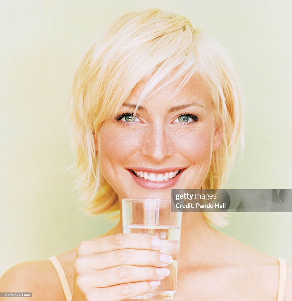 Young woman holding glass of water, smiling, close-up, portrait