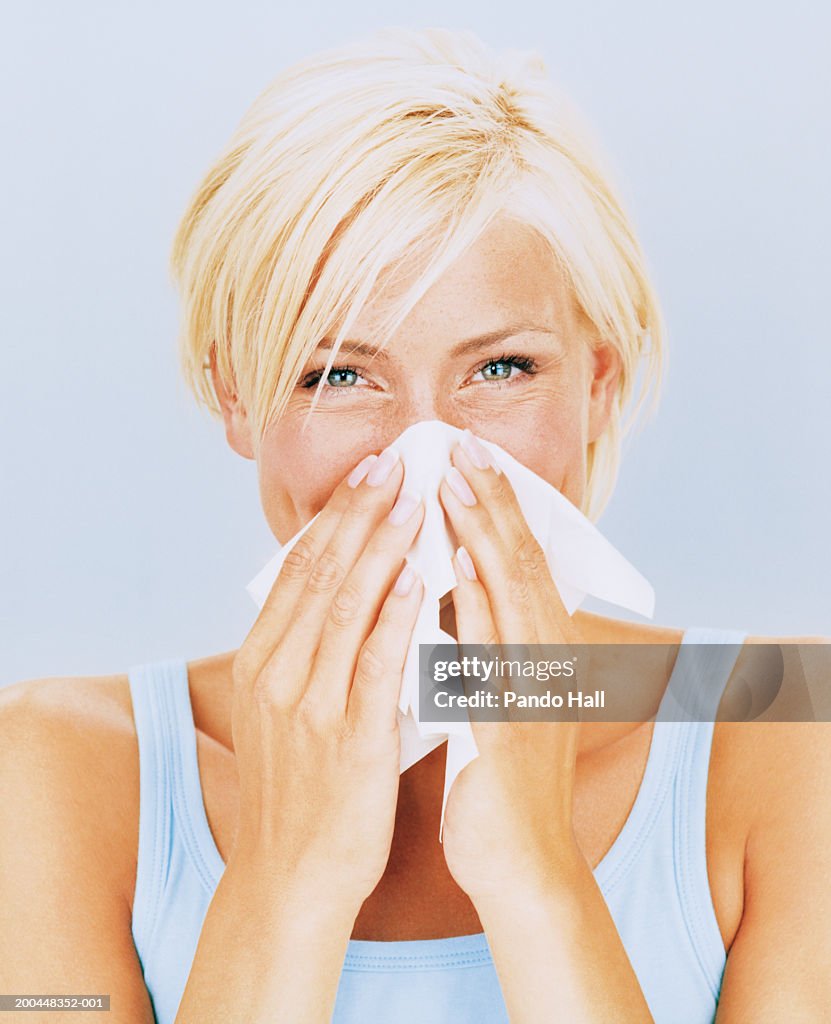 Young woman blowing nose, close-up, portrait