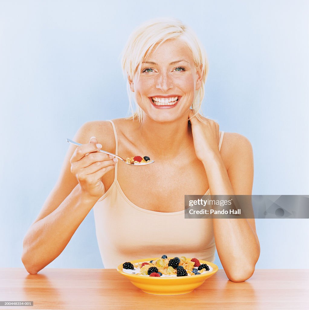 Young woman eating cereal and berries, smiling, portrait