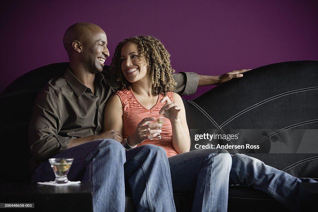 Man and woman with martinis sitting on sofa, smiling at one another