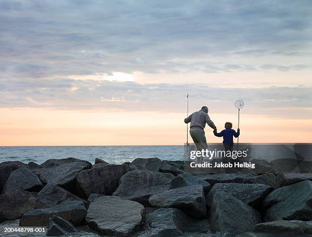 grandfather and grandson (4-6) walking on rocks with fishing equipment - grandad and grandkid stockfoto's en -beelden