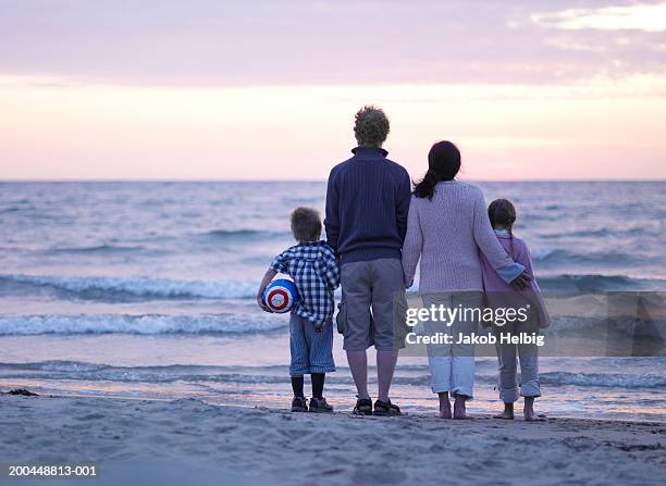 family standing on beach, boy holding ball, rear view, sunset - famille-avec-deux-enfants photos et images de collection