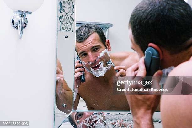 man shaving whilst using telephone (focus on reflection in mirror) - shaving cream stockfoto's en -beelden