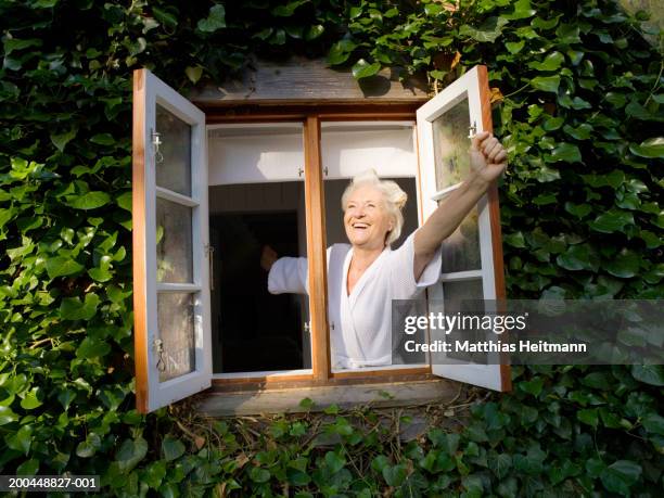 senior woman wearing rollers in hair opening window, smiling - open window stock pictures, royalty-free photos & images