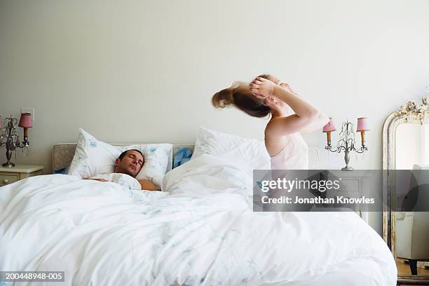 couple in bed, side view of woman throwing head back, man asleep - slaapkamer zijaanzicht stockfoto's en -beelden