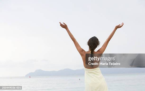 young woman standing on beach, arms raised, rear view - neckline stock pictures, royalty-free photos & images