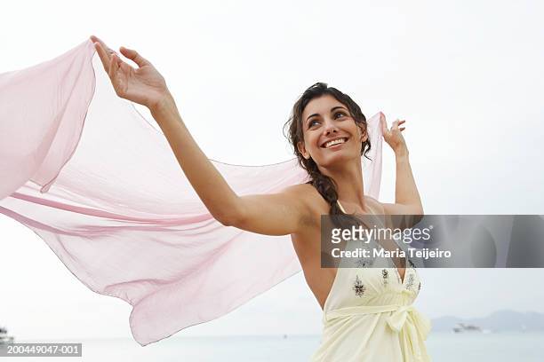 young womanon beach, holding pink stole to catch breeze - ショール ストックフォトと画像