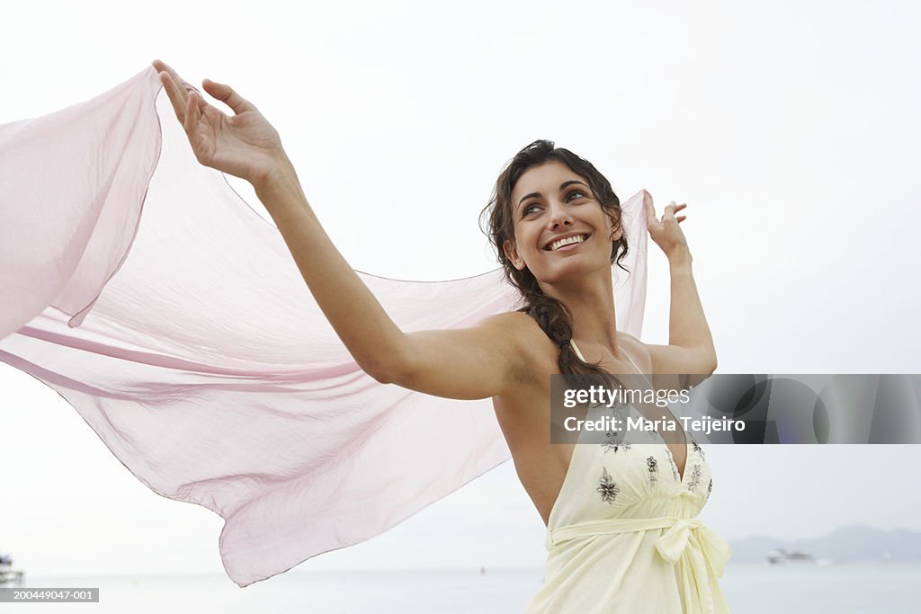 Young womanon beach, holding pink stole to catch breeze