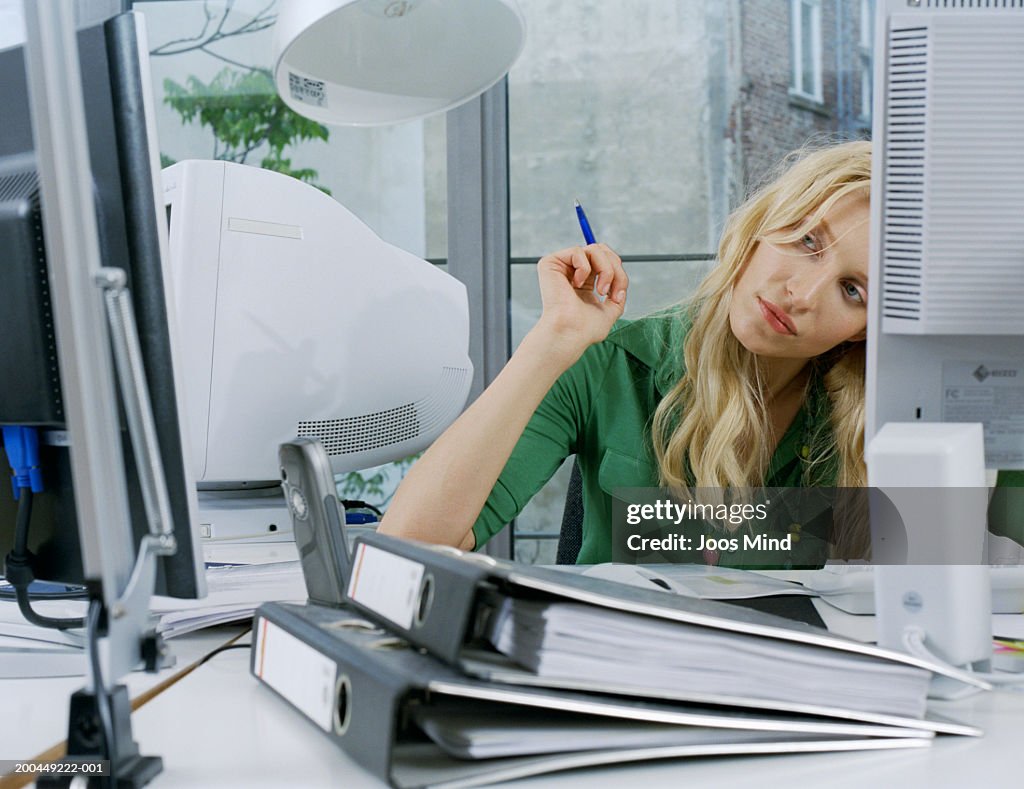 Young female office worker sitting at desk, looking to side