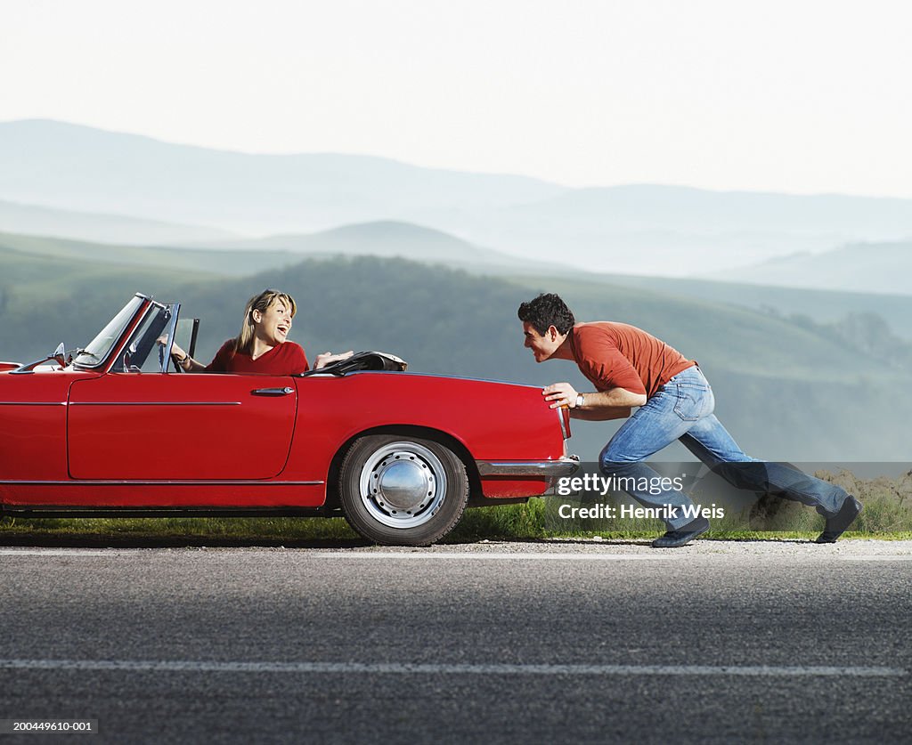 Woman in red convertible car being pushed by man, side view