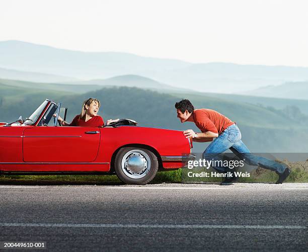 woman in red convertible car being pushed by man, side view - young couple red sunny stock pictures, royalty-free photos & images