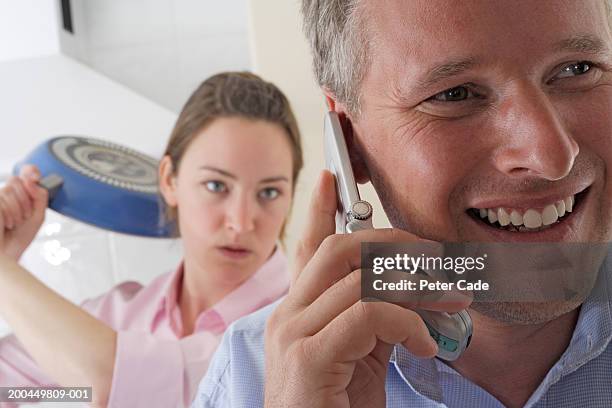 woman with frying pan about to hit man laughing on mobile phone - domestic violence men stock pictures, royalty-free photos & images