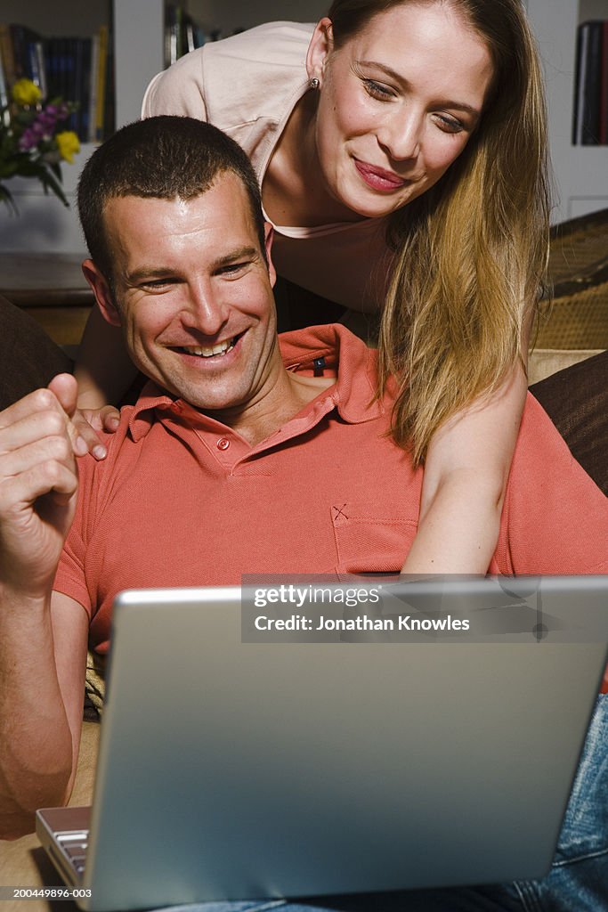 Couple using laptop, woman leaning over man's shoulder, smiling
