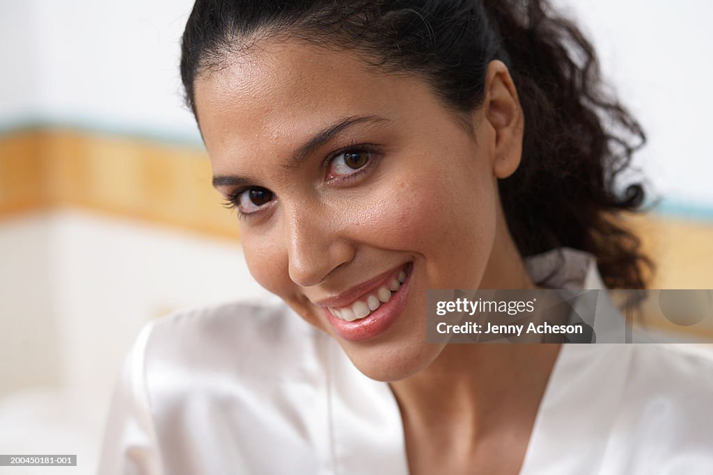 Young woman in bathroom, wearing bathrobe, smiling, portrait