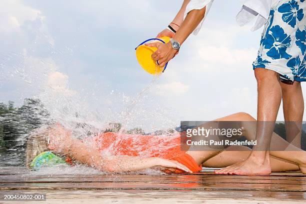 man pouring bucket of water over young woman lying down, side view - cooling down stock-fotos und bilder