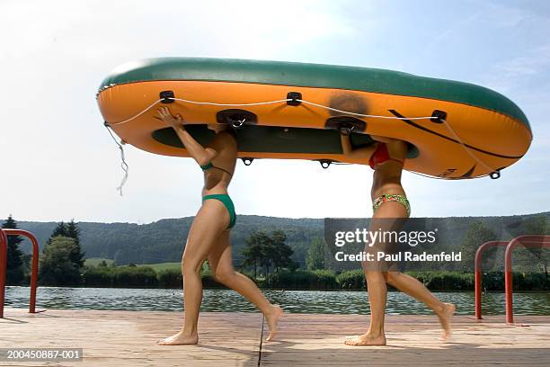 two women in bikinis carrying dinghy overhead, side view - rubber boat stock pictures, royalty-free photos & images