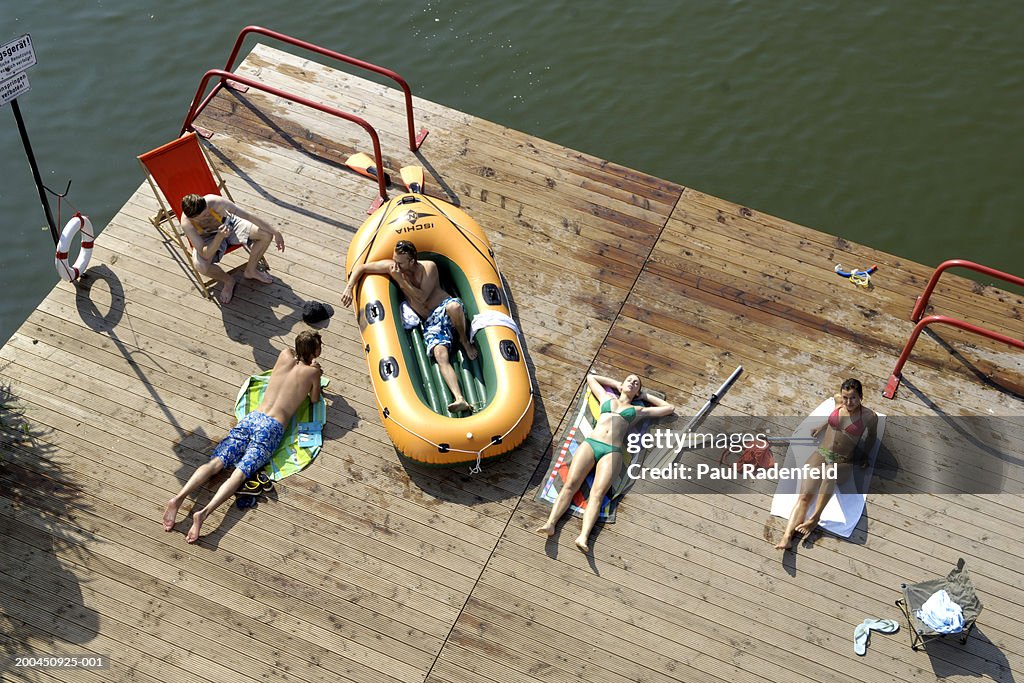 Five friends sunbathing on pier by lake, elevated view