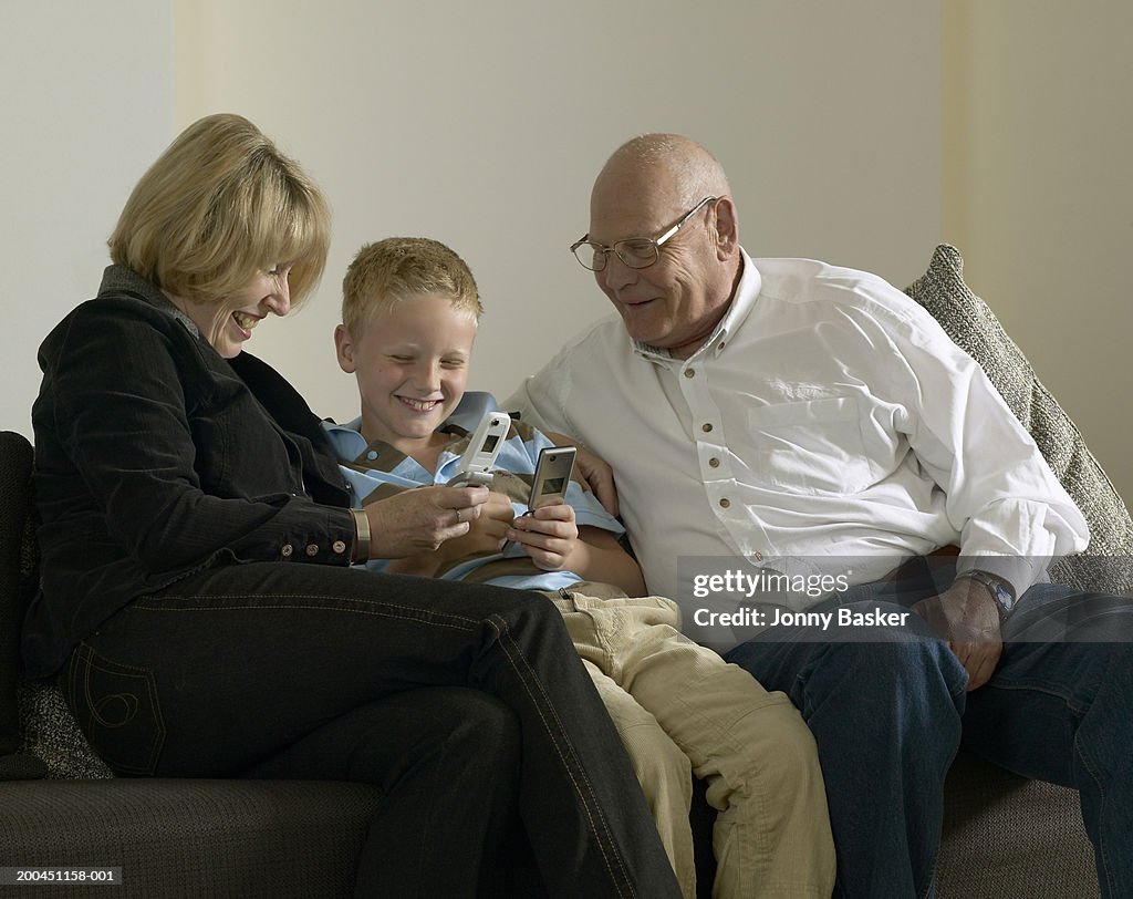 Boy (8-10) using mobile phone with grandparents, smiling