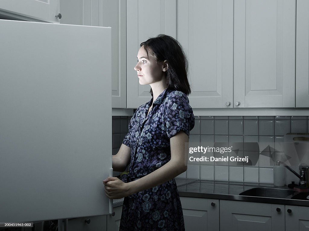 Woman opening fridge in kitchen, light illuminating face