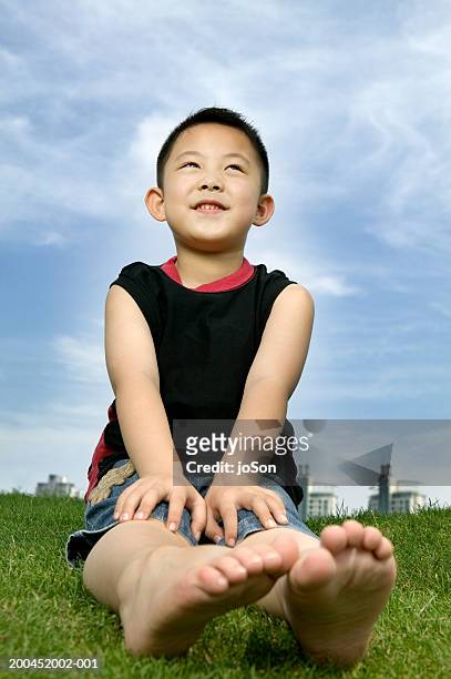 boy (4-6) sitting on lawn in park, ground view - boyshorts fotografías e imágenes de stock