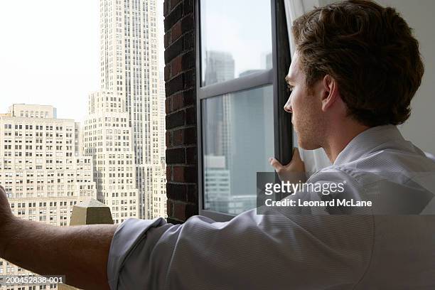 young businessman opening window, facing office buildings in cityscape - hemd aufreißen stock-fotos und bilder