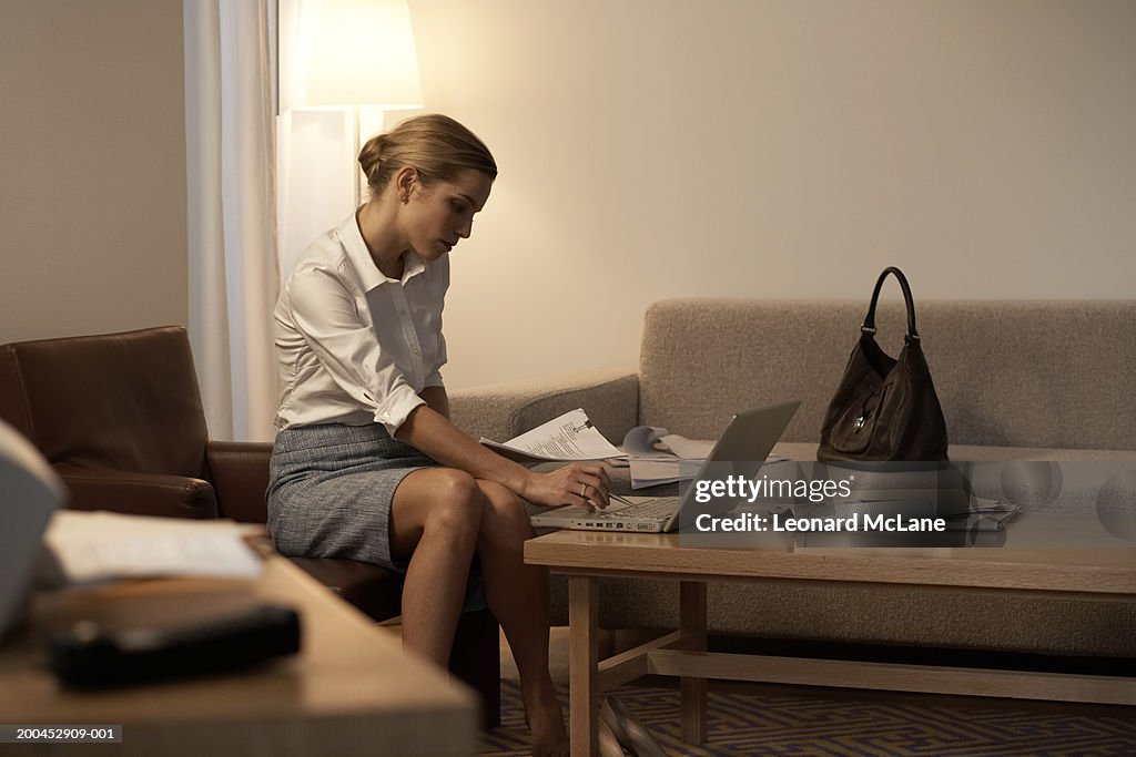 Businesswoman sitting in hotel room using laptop on coffee table