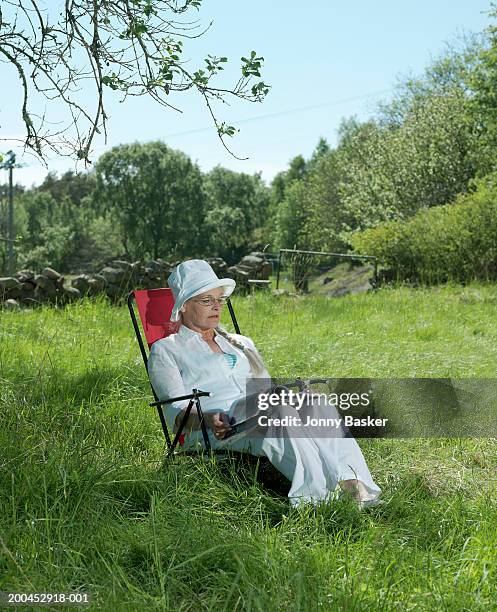 mature woman reading in garden chair in field - leesbril stockfoto's en -beelden