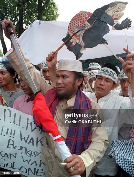 An Indonesia protester shows a sword which is covered with an Indonesia flag, while another protester holds a traditional Java puppet called "Semar,"...