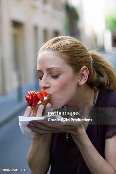 young woman eating strawberry-topped cake, outdoors, close-up - erdbeerkuchen stock-fotos und bilder