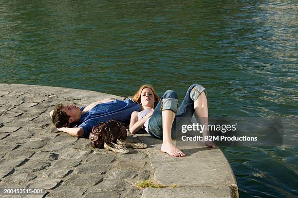 young couple lying at edge of quay, woman resting head on man's leg - quayside stock pictures, royalty-free photos & images