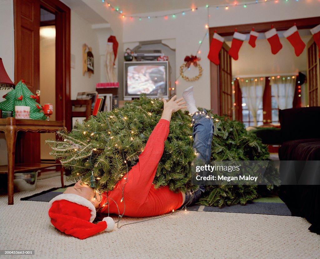 Man lying  under Cristmas tree tangled in string of lights