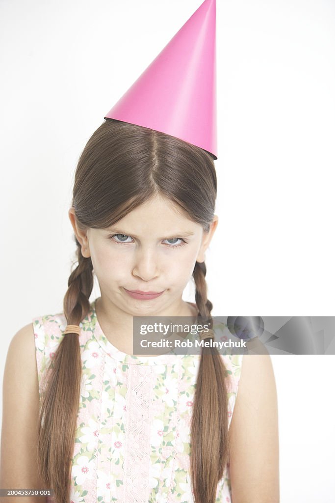 Girl (6-8) wearing party hat, making face, portrait