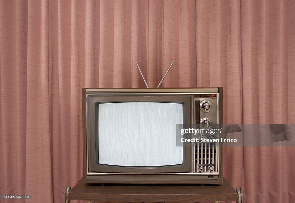 Old television on stand, in front of curtain
