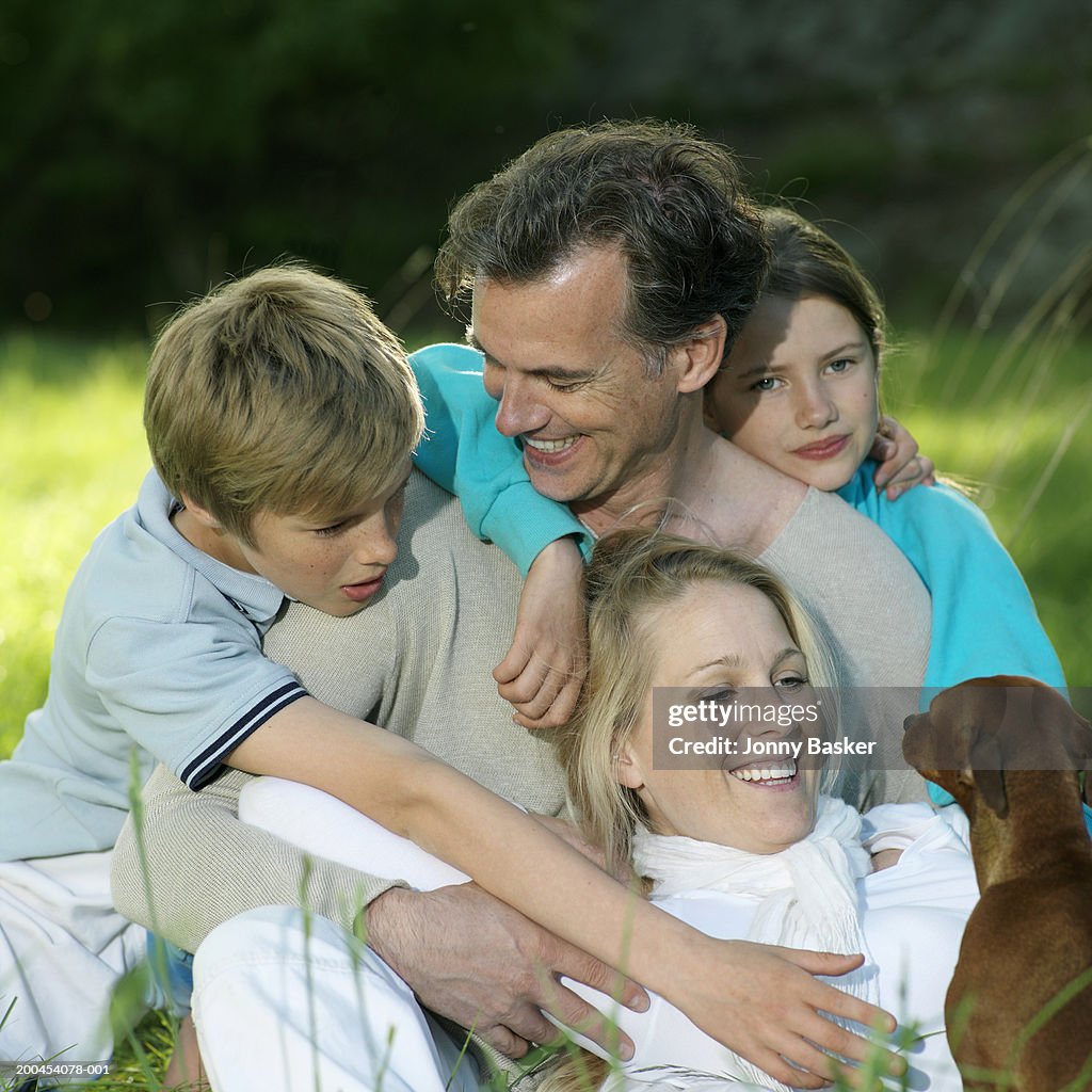 Family sitting in field with pet dog, smiling