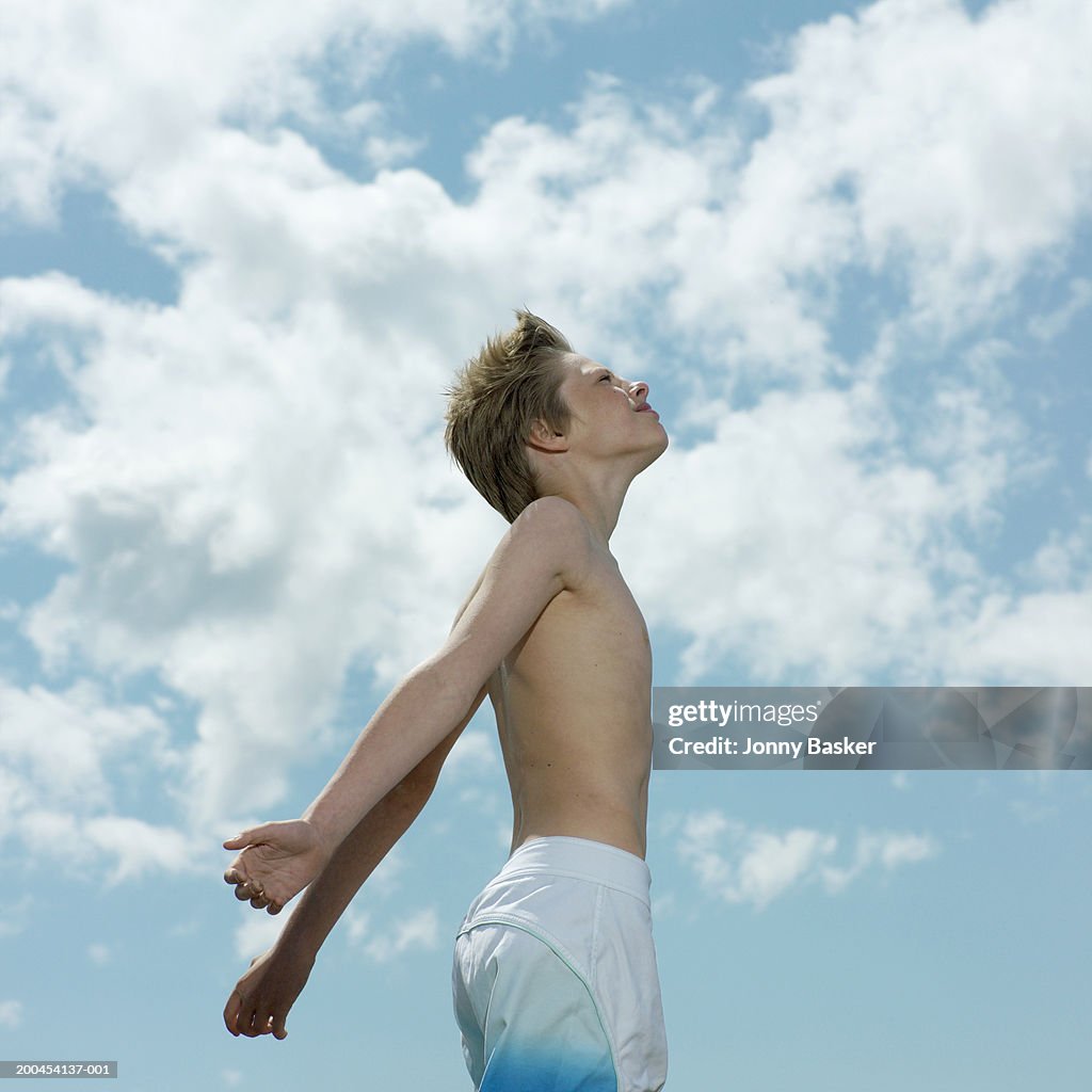 Boy (13-15) in shorts under cloudy sky, looking up, side view
