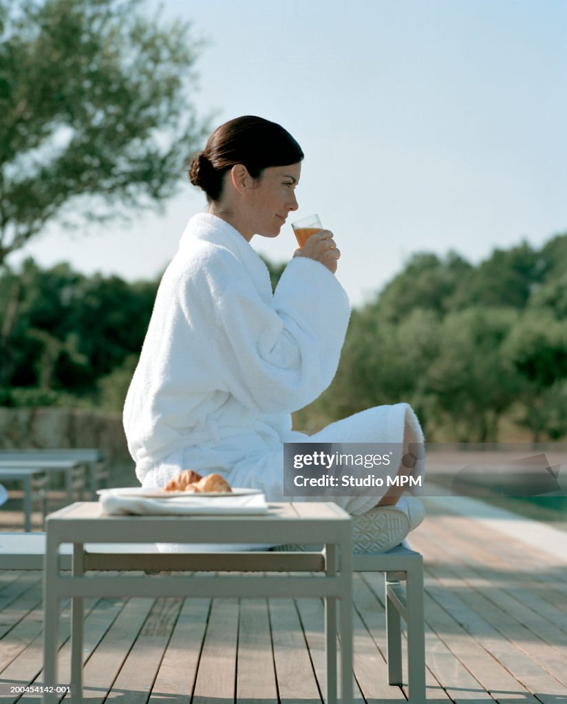 Young woman wearing dressing gown having breakfast by swimming pool